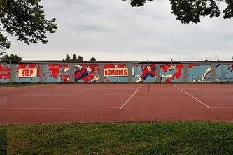 Auf lange Mauer vor Tennisplatz: Graffiti zeigt einen Para-Sprinter umgeben von angedeutetem Blut und dem Schriftzug Stop Bombing Civilians